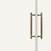 Antique brass double-sided door pull with vertical ribbed handles mounted on a white surface.